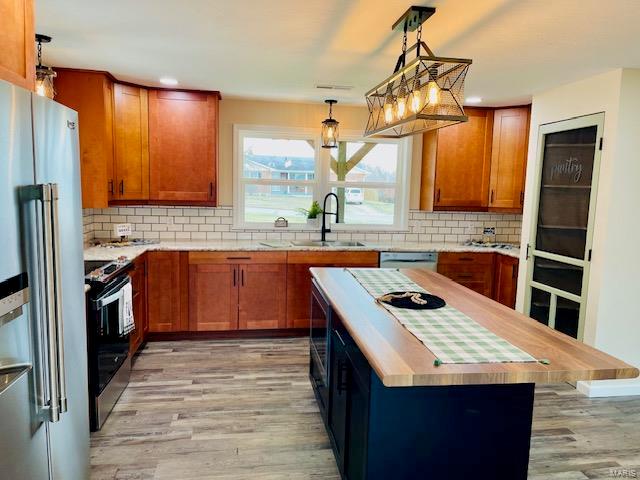 kitchen with appliances with stainless steel finishes, tasteful backsplash, sink, and light hardwood / wood-style flooring