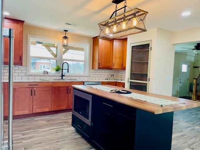 kitchen with stainless steel microwave, a center island, backsplash, light hardwood / wood-style floors, and ceiling fan with notable chandelier