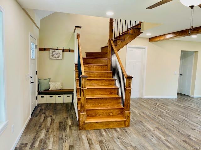 stairs featuring wood-type flooring, ceiling fan, and beamed ceiling