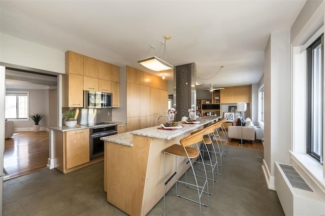 kitchen with a kitchen bar, light stone counters, light brown cabinets, a kitchen island, and stainless steel appliances