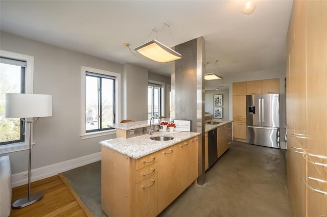 kitchen featuring light brown cabinetry, appliances with stainless steel finishes, a sink, and light stone counters