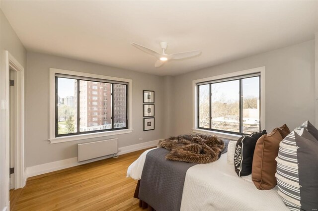 bedroom with light wood-style floors, radiator heating unit, baseboards, and a ceiling fan