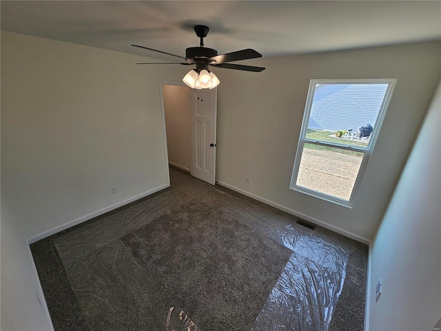 spare room with ceiling fan and dark colored carpet