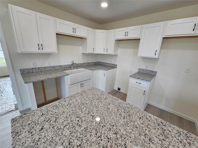 kitchen featuring sink, white cabinets, hardwood / wood-style floors, and light stone countertops