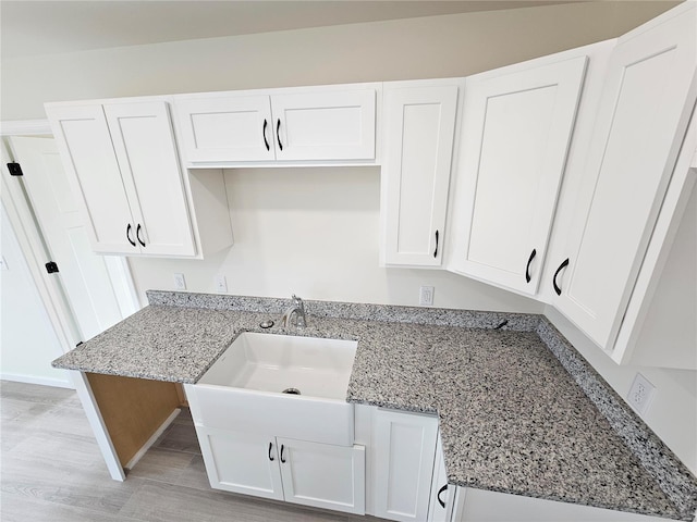 kitchen with sink, white cabinetry, light stone counters, and light hardwood / wood-style floors