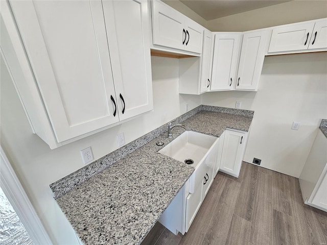 kitchen with sink, white cabinetry, light wood-type flooring, and light stone counters