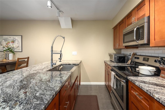 kitchen with backsplash, rail lighting, dark tile flooring, stone countertops, and appliances with stainless steel finishes