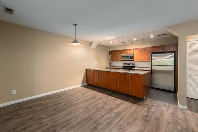 kitchen with light stone countertops, backsplash, rail lighting, hanging light fixtures, and appliances with stainless steel finishes