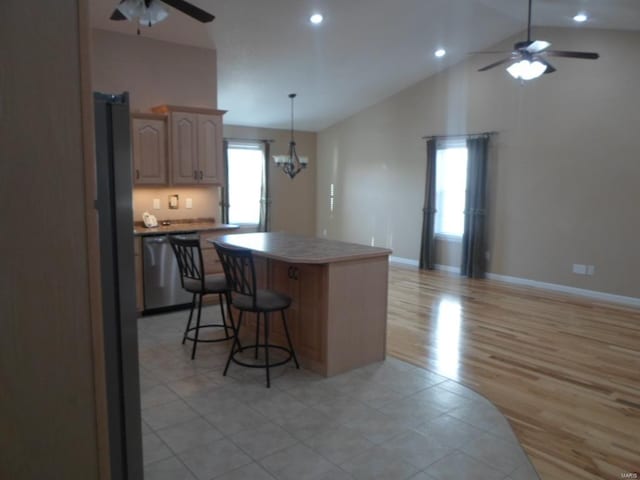 kitchen featuring a kitchen island, a kitchen breakfast bar, stainless steel dishwasher, light tile flooring, and ceiling fan with notable chandelier