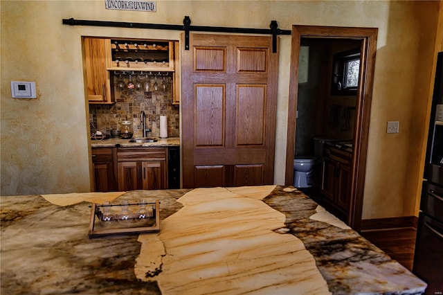 kitchen with sink, backsplash, a barn door, dark hardwood / wood-style floors, and light stone countertops