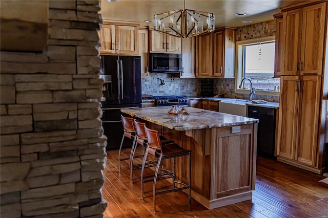 kitchen featuring black appliances, backsplash, decorative light fixtures, a kitchen island, and hardwood / wood-style flooring