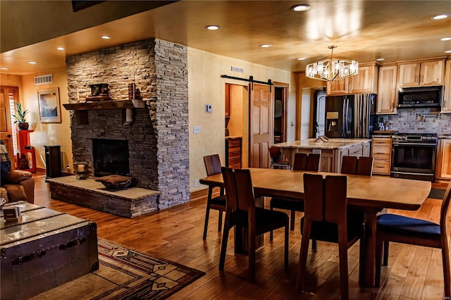 dining space with a fireplace, wood-type flooring, a notable chandelier, and a barn door