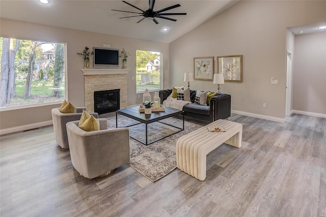 living room with wood-type flooring, a stone fireplace, high vaulted ceiling, and ceiling fan