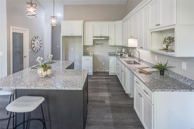 kitchen with white cabinets, sink, a kitchen island, decorative light fixtures, and dark wood-type flooring