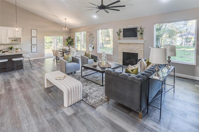 living area with baseboards, ceiling fan, wood finished floors, a fireplace, and high vaulted ceiling