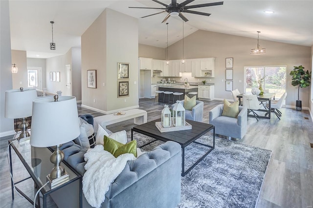 living area with high vaulted ceiling, light wood finished floors, a ceiling fan, and baseboards