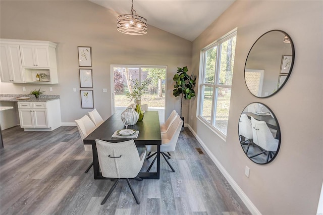 dining room featuring dark wood finished floors, visible vents, vaulted ceiling, and baseboards