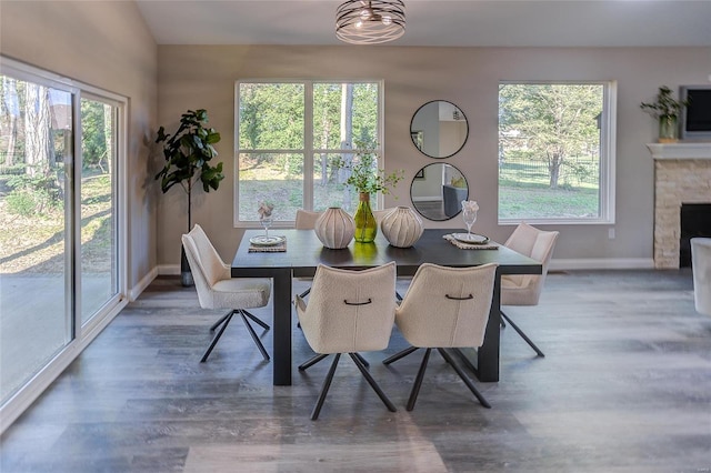 dining space featuring dark wood-style floors, a stone fireplace, and baseboards