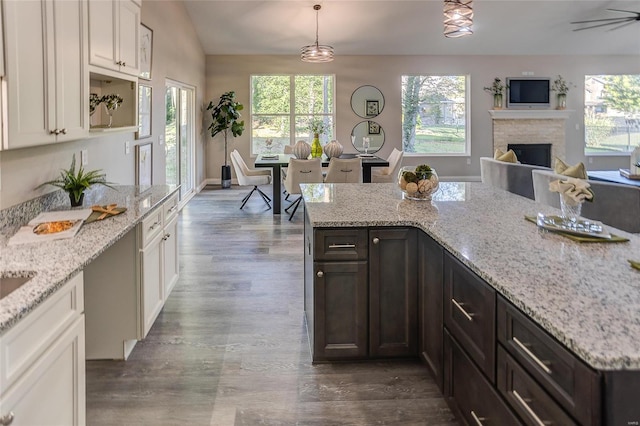 kitchen featuring dark brown cabinetry, white cabinets, light stone counters, hanging light fixtures, and a fireplace