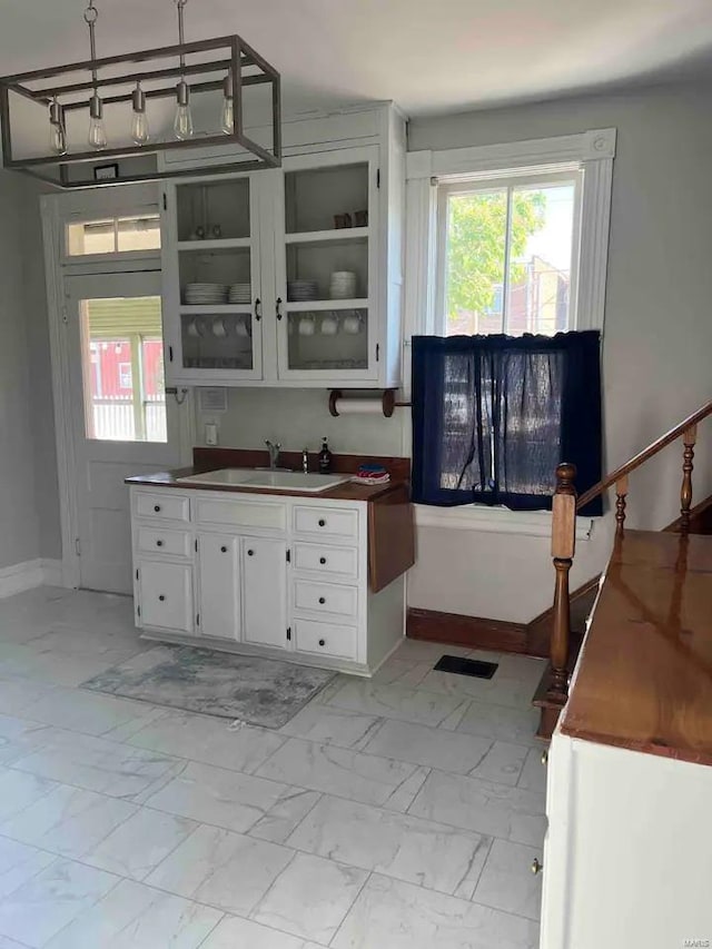 kitchen featuring pendant lighting, white cabinetry, light tile floors, and sink