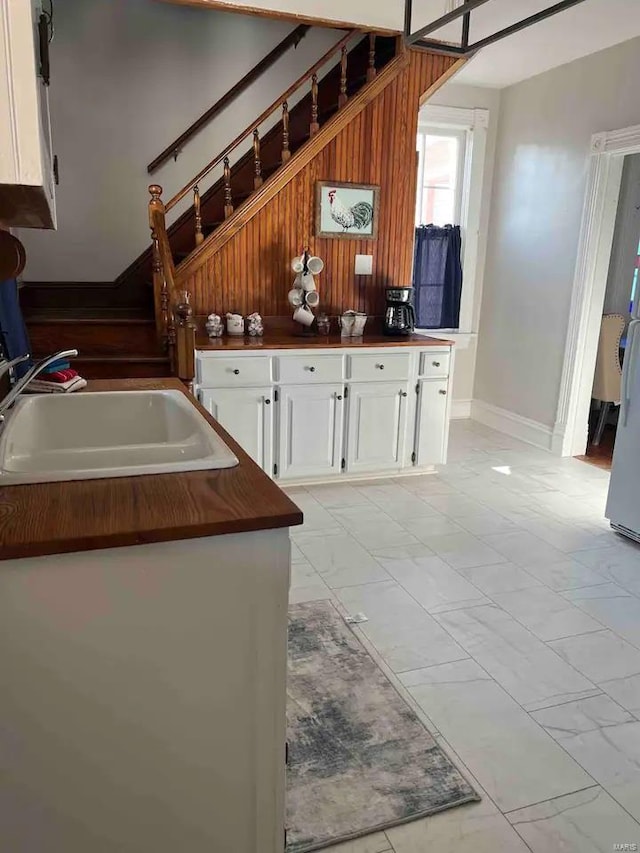 kitchen featuring wooden walls, sink, white cabinetry, and light tile floors