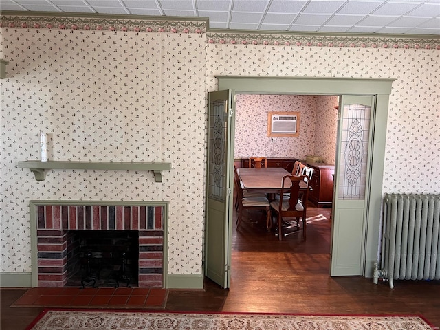 interior space with dark hardwood / wood-style floors, a brick fireplace, a paneled ceiling, a wall mounted air conditioner, and radiator heating unit