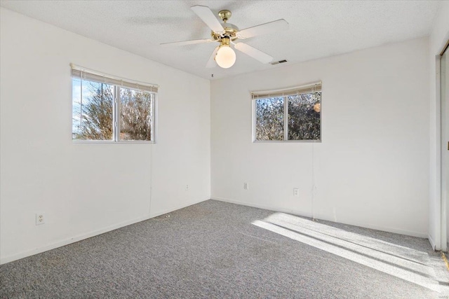 carpeted empty room featuring ceiling fan, a healthy amount of sunlight, and a textured ceiling