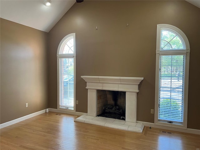 unfurnished living room with high vaulted ceiling, a tile fireplace, and light hardwood / wood-style flooring