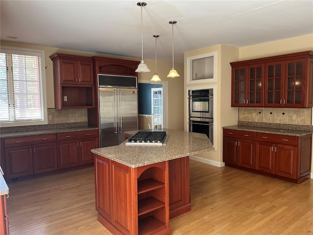 kitchen with pendant lighting, a kitchen island, tasteful backsplash, appliances with stainless steel finishes, and light wood-type flooring