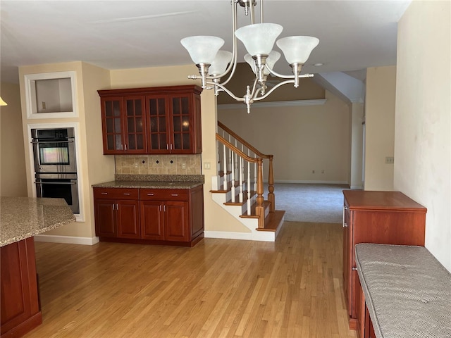 kitchen with decorative light fixtures, stainless steel double oven, an inviting chandelier, light carpet, and tasteful backsplash