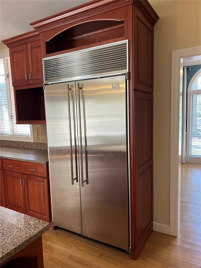 kitchen with light hardwood / wood-style flooring, backsplash, built in fridge, and dark stone countertops