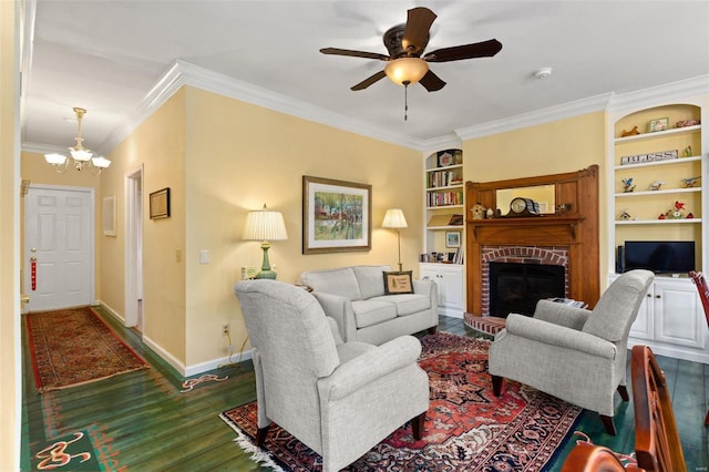 living room featuring ceiling fan with notable chandelier, built in features, dark wood-type flooring, ornamental molding, and a brick fireplace