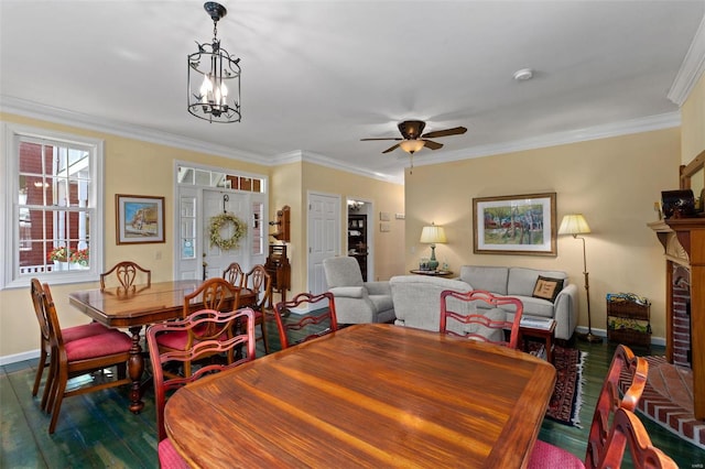 dining area featuring ceiling fan with notable chandelier, dark wood-type flooring, ornamental molding, and a fireplace