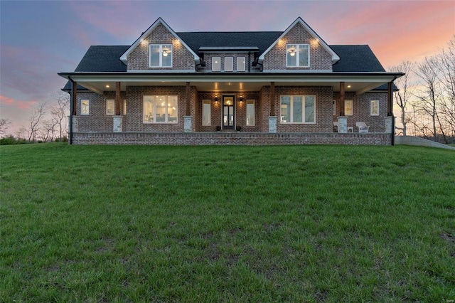 back house at dusk with a lawn and covered porch