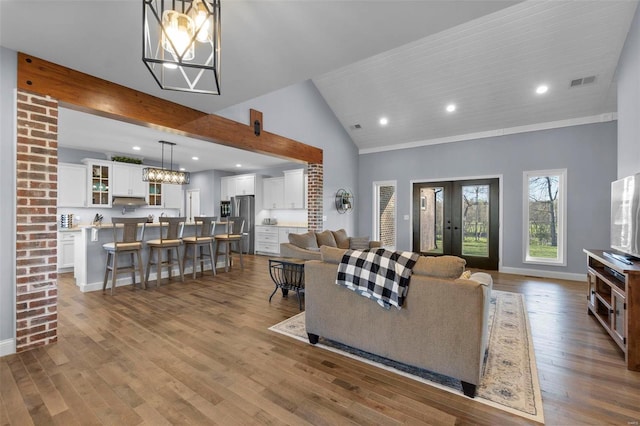 living room featuring a notable chandelier, brick wall, light hardwood / wood-style floors, and vaulted ceiling