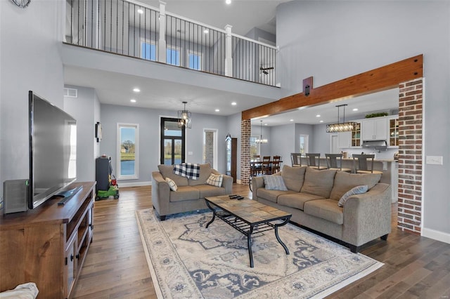 living room with brick wall, a high ceiling, a notable chandelier, and dark hardwood / wood-style flooring