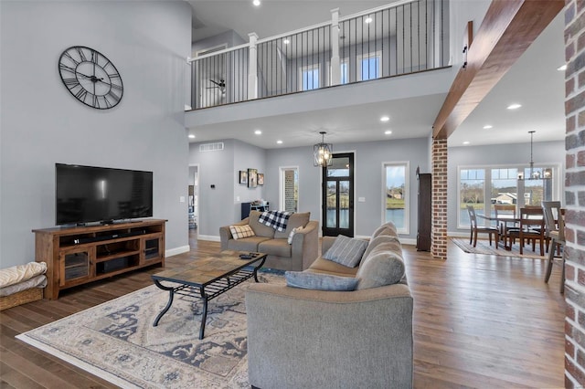 living room with a chandelier, a high ceiling, brick wall, and dark wood-type flooring