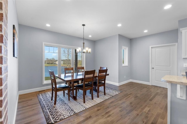 dining room featuring brick wall, a water view, a notable chandelier, and dark wood-type flooring