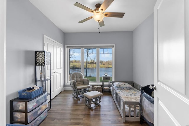 sitting room featuring a water view, dark wood-type flooring, and ceiling fan