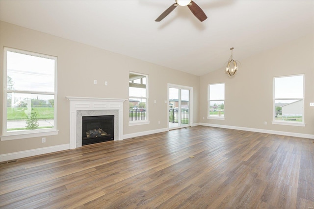 unfurnished living room featuring a wealth of natural light, a premium fireplace, ceiling fan with notable chandelier, and dark hardwood / wood-style floors