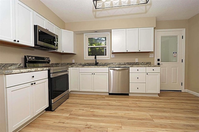 kitchen with stainless steel appliances, sink, white cabinets, a textured ceiling, and light hardwood / wood-style floors