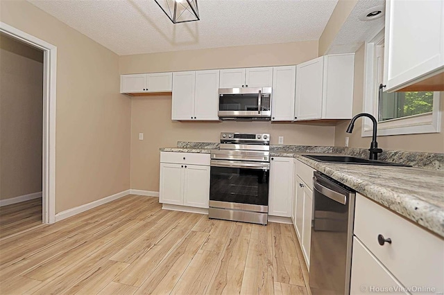 kitchen with light hardwood / wood-style floors, appliances with stainless steel finishes, a textured ceiling, and white cabinets