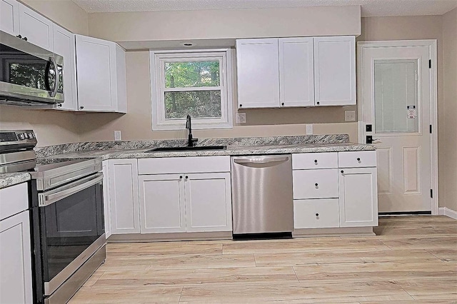 kitchen featuring appliances with stainless steel finishes, sink, a textured ceiling, white cabinetry, and light hardwood / wood-style floors