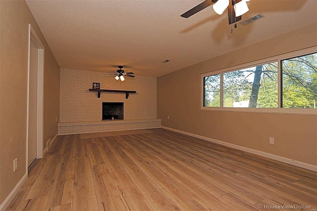 unfurnished living room featuring a brick fireplace, a textured ceiling, wood-type flooring, and ceiling fan