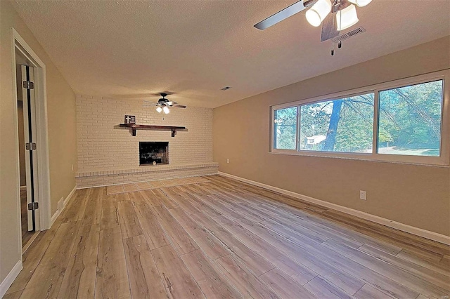 unfurnished living room featuring a brick fireplace, a textured ceiling, and light hardwood / wood-style floors