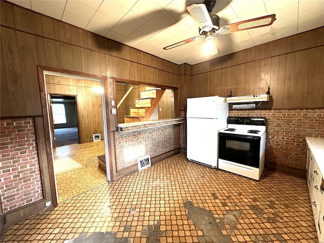 kitchen featuring ceiling fan, wooden walls, white appliances, and light tile flooring