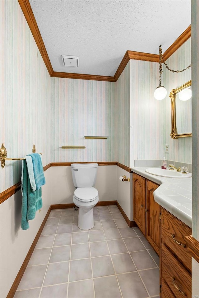 bathroom with tile patterned flooring, toilet, ornamental molding, vanity, and a textured ceiling