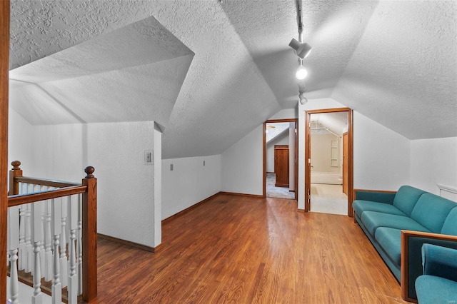 additional living space with vaulted ceiling, hardwood / wood-style flooring, and a textured ceiling