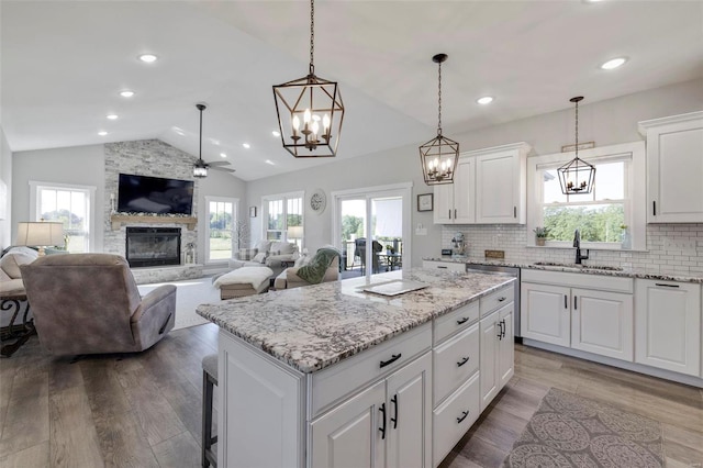 kitchen featuring hardwood / wood-style floors, a stone fireplace, a center island, and decorative light fixtures