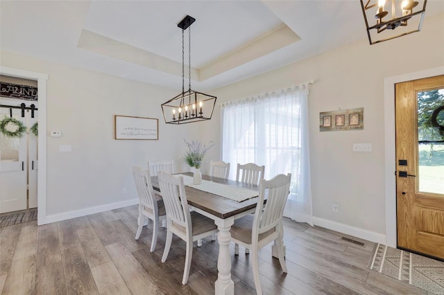 dining area featuring light hardwood / wood-style floors, a chandelier, and a tray ceiling